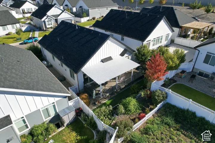 Aerial perspective of a single-story residence featuring vertical siding, a dark shingled roof, a covered concrete patio, and a fenced backyard with landscaped garden beds