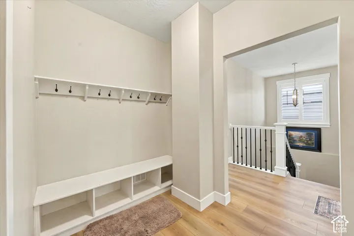 Built-in white storage bench with integrated shelving, wall-mounted white coat rack with black metal hooks, wood-finish flooring, and black metal stair balusters