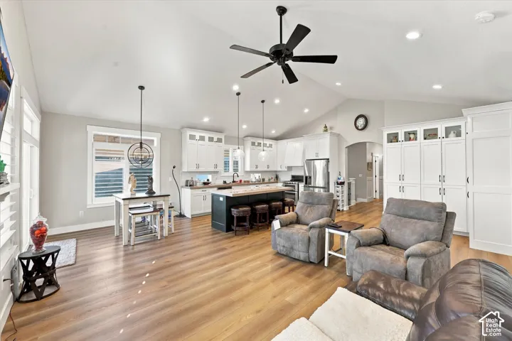 Vaulted ceilings, wood-finish flooring, white shaker-style cabinetry, a contrasting kitchen island with countertop seating, and recessed lighting