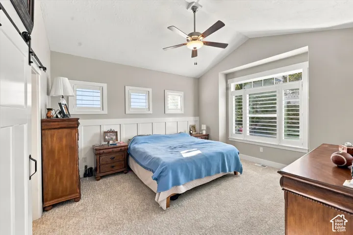 Vaulted ceiling featuring a central lighted ceiling fan, decorative wainscoting, multiple grid-style windows, and a sliding barn-style door
