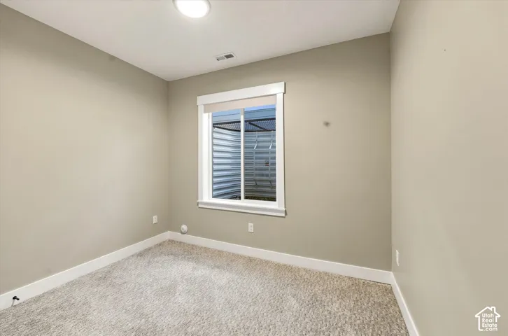 Neutral-toned interior space featuring wall-to-wall carpeting, a window with white trim, and an egress window well