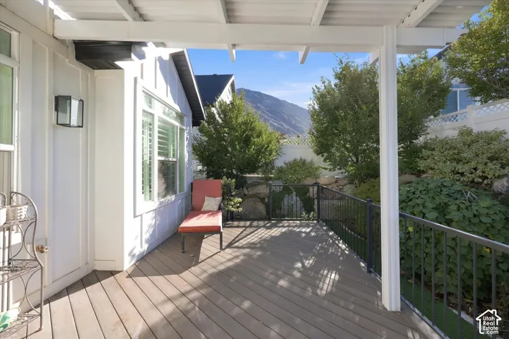 Covered patio featuring composite decking, white pergola framing, black metal railing, and mountain backdrop
