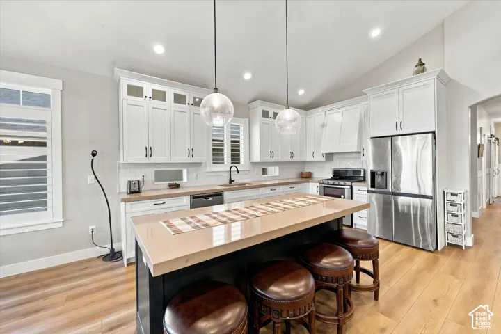 Kitchen featuring white cabinetry with glass-panel uppers, contrasting dark island, solid surface countertops, wood-finish flooring, and pendant lighting