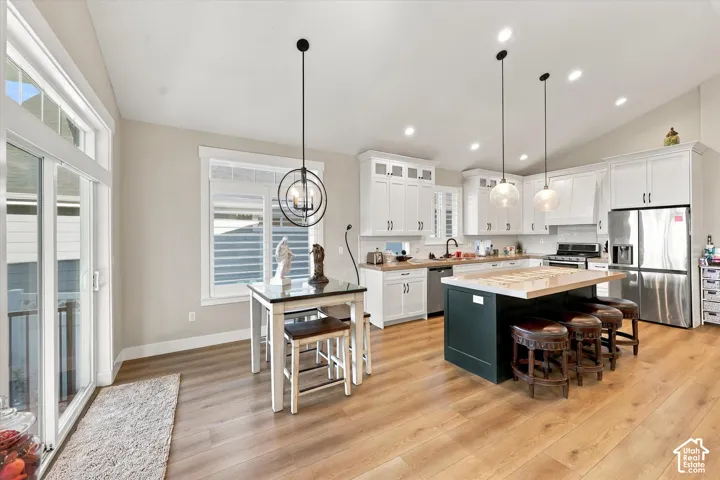 Kitchen featuring white shaker-style cabinetry, center island with stone countertop, wood-finish flooring, vaulted ceilings, and stainless-steel appliances