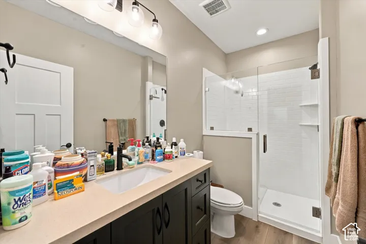 Dark-toned vanity with a light-colored countertop, integrated undermount sink, matte black faucet, glass-enclosed shower with white subway tiling, and wood-finish flooring