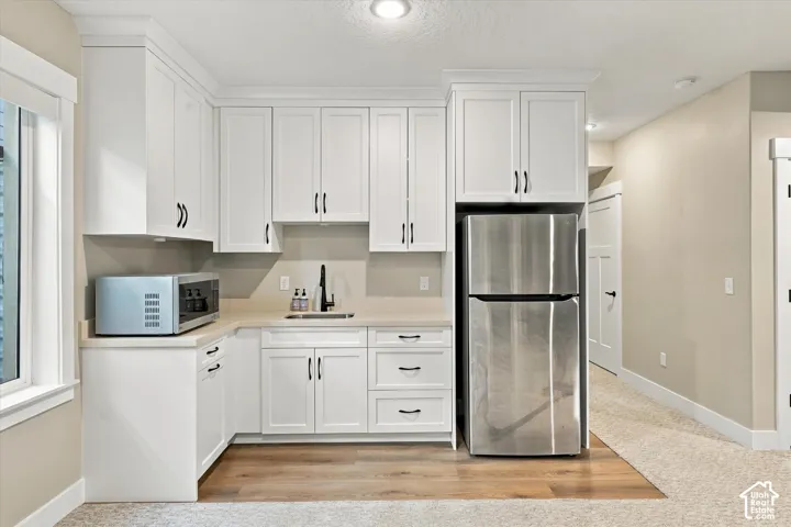 Kitchenette featuring white Shaker-style cabinetry, matte black hardware, solid-surface countertops, inset sink with a high-arch faucet, and wood-finish flooring