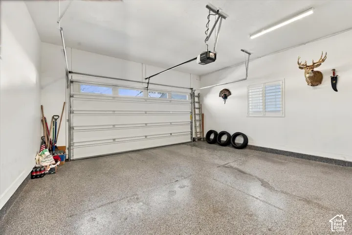 Finished garage featuring an epoxy-coated floor, automatic overhead door with integrated windows, high-output LED lighting, and plantation shutter window treatment