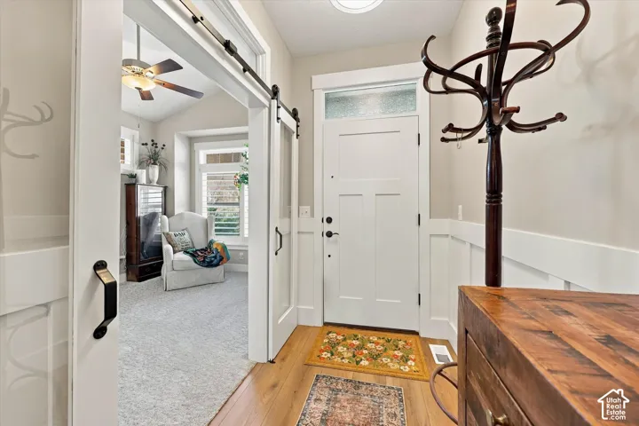 Entryway featuring wood-finish flooring, white board-and-batten wainscoting, a paneled door with a glass transom, and a sliding door on an exposed metal track