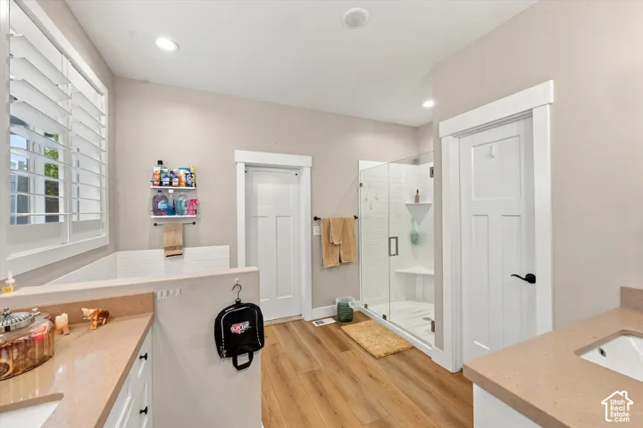 Bathroom featuring wood-finish flooring, a glass-enclosed shower with subway tile surround, quartz-surfaced countertops, plantation shutters, and multi-panel interior doors