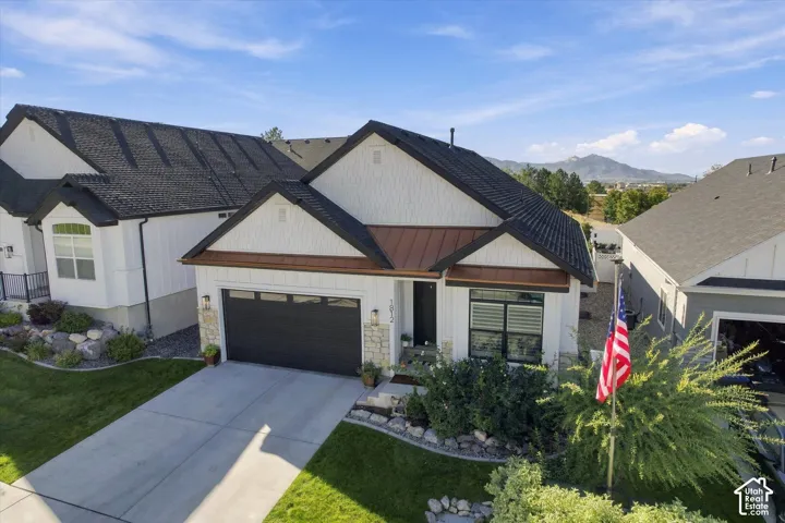 Contemporary exterior featuring vertical siding, stone veneer accents, metal roofing details, and a multi-panel garage door, set against a mountain backdrop
