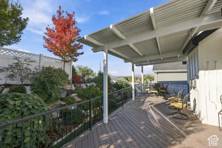 Covered composite deck featuring a metal railing, corrugated metal roof, tiered rock landscaping, and white lattice-topped privacy fencing
