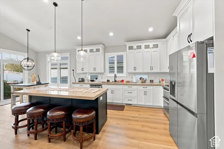Kitchen featuring white shaker-style cabinetry, quartz countertops, a contrasting dark-finished center island, wood-finish flooring, and glass pendant lighting