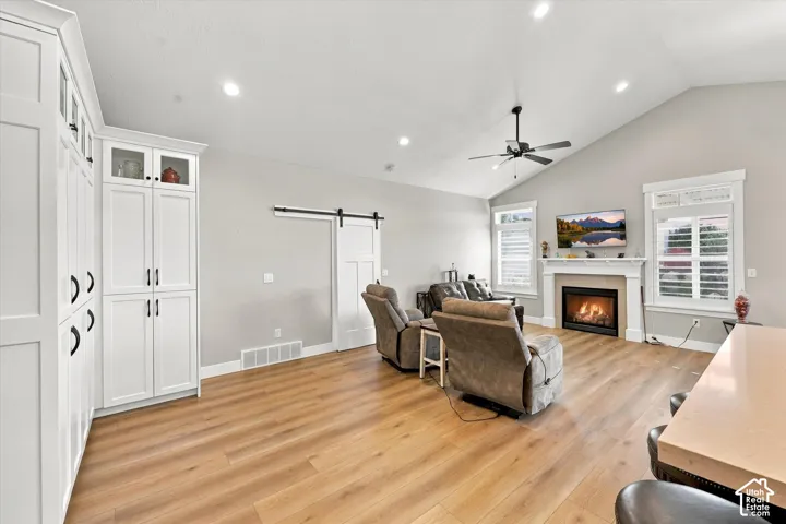 Vaulted ceilings, built-in floor-to-ceiling cabinetry, wood-finish flooring, sliding barn door, and fireplace with a decorative mantel