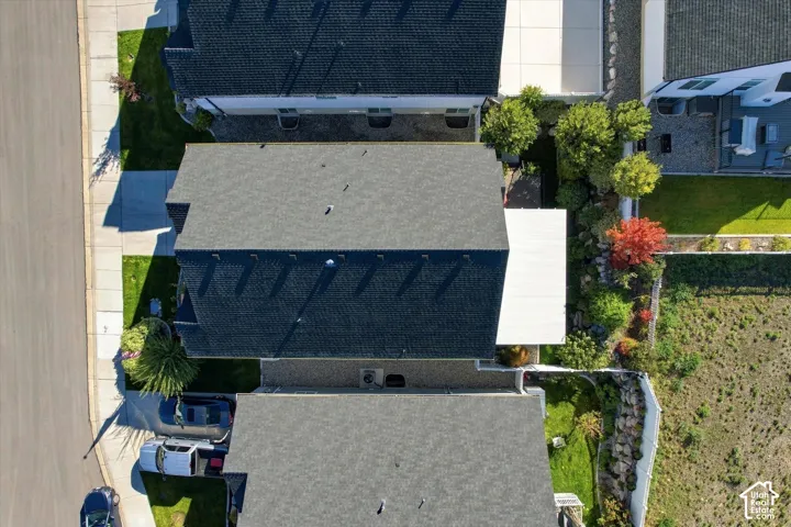 Aerial perspective of property featuring an asphalt shingle roof, a paved driveway, a white pergola, tiered landscape retaining walls, and mature perimeter trees