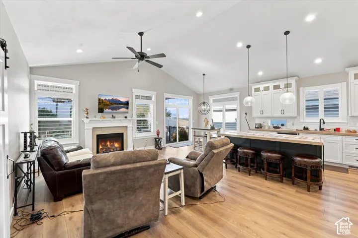 Open-concept kitchen and living area featuring vaulted ceilings, wood-finish flooring, a fireplace with a decorative mantel, and an oversized island with pendant lighting