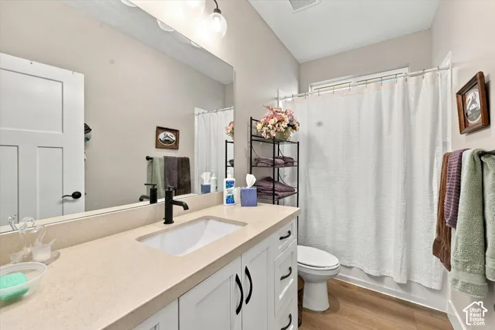 Bathroom featuring white cabinetry, solid-surface countertop with an integrated rectangular sink, matte black faucet, full-width mirror, and wood-finish flooring