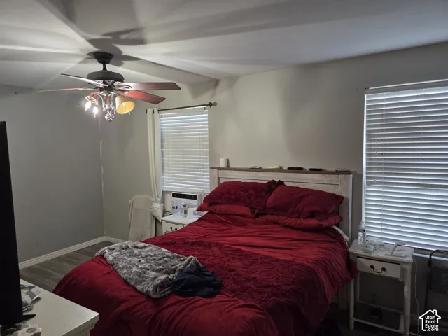 Room featuring wood-finish flooring, dual windows with horizontal blinds, and a multi-light ceiling fan