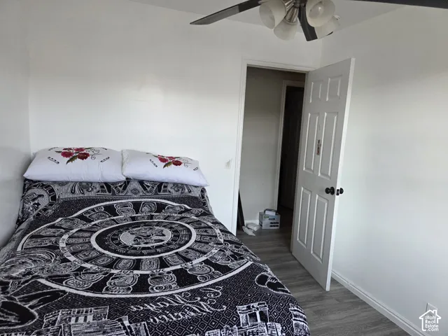 Room featuring wood-finish flooring, a six-panel interior door with matte black hardware, and a ceiling fan with multi-directional light fixtures