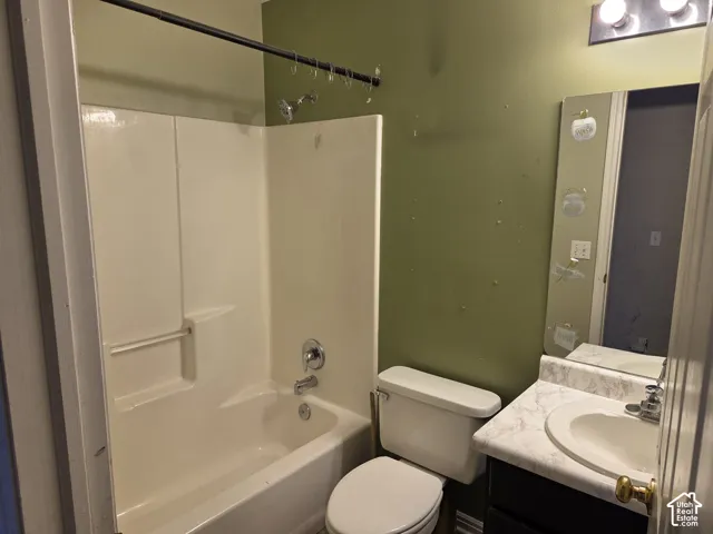 Full-height shower and tub surround with integrated shelving, vanity featuring a stone-patterned countertop and undermount sink, and wall-mounted vanity mirror with integrated lighting