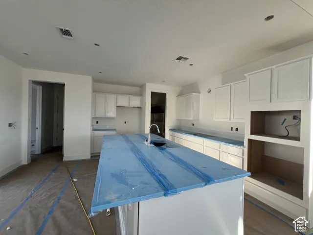 Kitchen featuring white Shaker-style cabinetry, a central island with an undermount sink, recessed lighting, and built-in appliance cabinetry