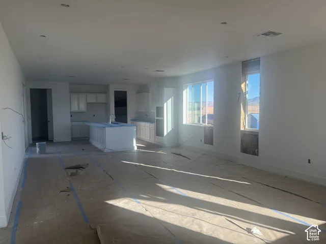 Open-concept kitchen featuring white cabinetry, a center island with an integrated sink, built-in wall oven, and recessed lighting