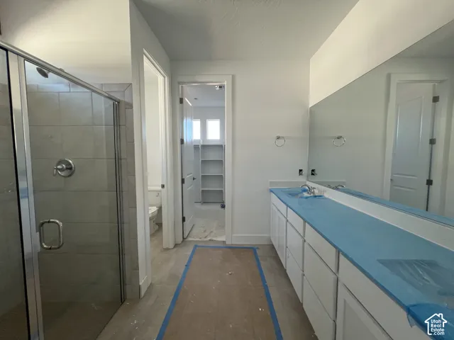 Bathroom featuring a double-sink vanity with cabinetry, large wall-mounted mirror, walk-in shower with tile surround and glass enclosure, and tile flooring