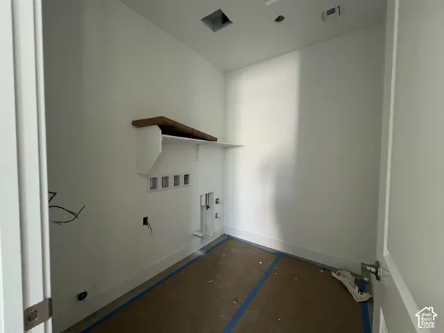 Utility room featuring white walls, a built-in wooden shelf, and dedicated plumbing and electrical hookups