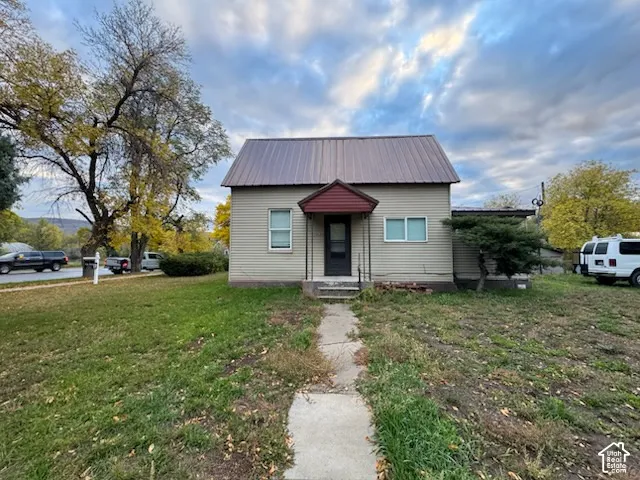 Single-story exterior featuring light-toned horizontal siding, a peaked metal roof, an entrance portico with a gable roof, and a concrete walkway