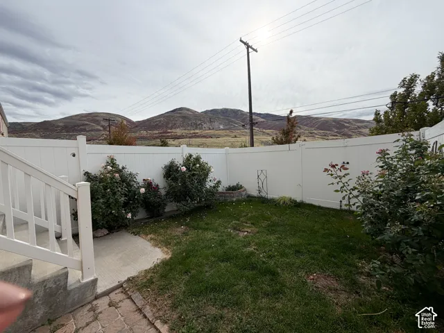 Enclosed backyard featuring a vinyl privacy fence, concrete paver patio, mature rose bushes, and a mountain backdrop