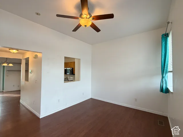 High ceilings featuring a central ceiling fan with integrated lighting, wood-finish flooring, and a passthrough wall opening