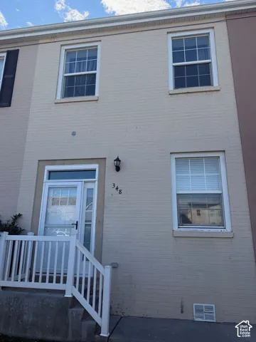 Light-colored brick exterior featuring a white storm door, transom window, white vertical balustrade, and dual-pane windows with muntins