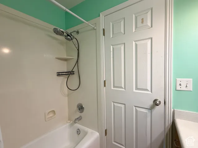 Bathtub with integrated wall surround, handheld shower fixture, and polished metal hardware