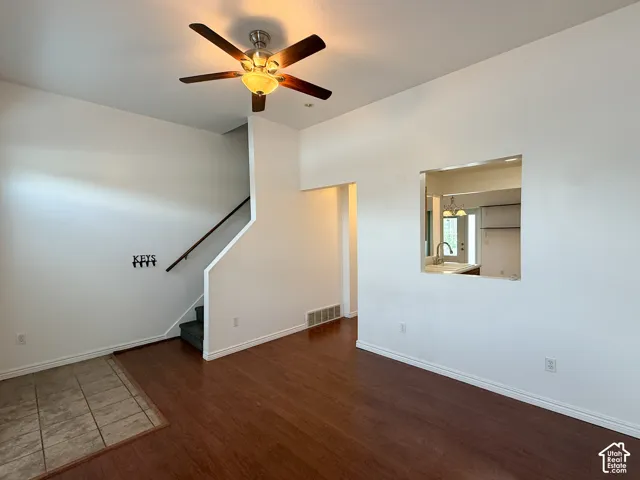 High-ceilinged room featuring wood-finish flooring, ceramic tile entry, multi-blade ceiling fan, and a built-in architectural pass-through