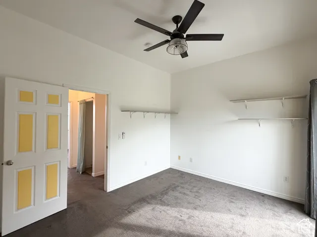Neutral-toned carpeted flooring, vaulted ceilings, matte black ceiling fan with integrated lighting, and multiple tiers of built-in wall shelving