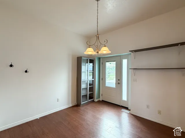 Wood-finish flooring, three-light metal chandelier, built-in display cabinetry, glass-panel entry door, and wall-mounted shelving