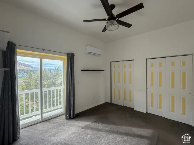 Sliding glass door opening to a balcony, ceiling fan with integrated lighting, wall-mounted ductless air conditioning unit, and two sets of double-door closets
