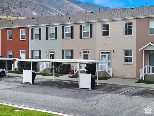Multi-story brick exterior featuring covered carports, white-railed entry stairs, and mountain backdrop