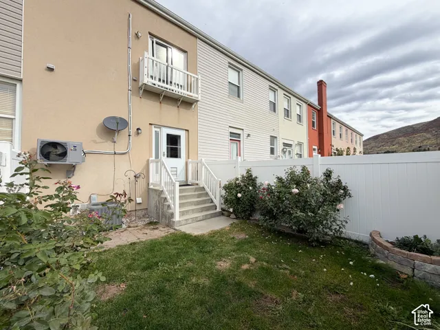Rear exterior featuring a private fenced yard, concrete stairs with railings, second-story balcony, and established shrubbery against a mountain backdrop