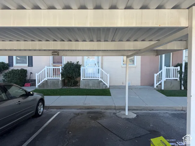 Covered carport featuring a metal roof structure, concrete walkways, and exterior white railings