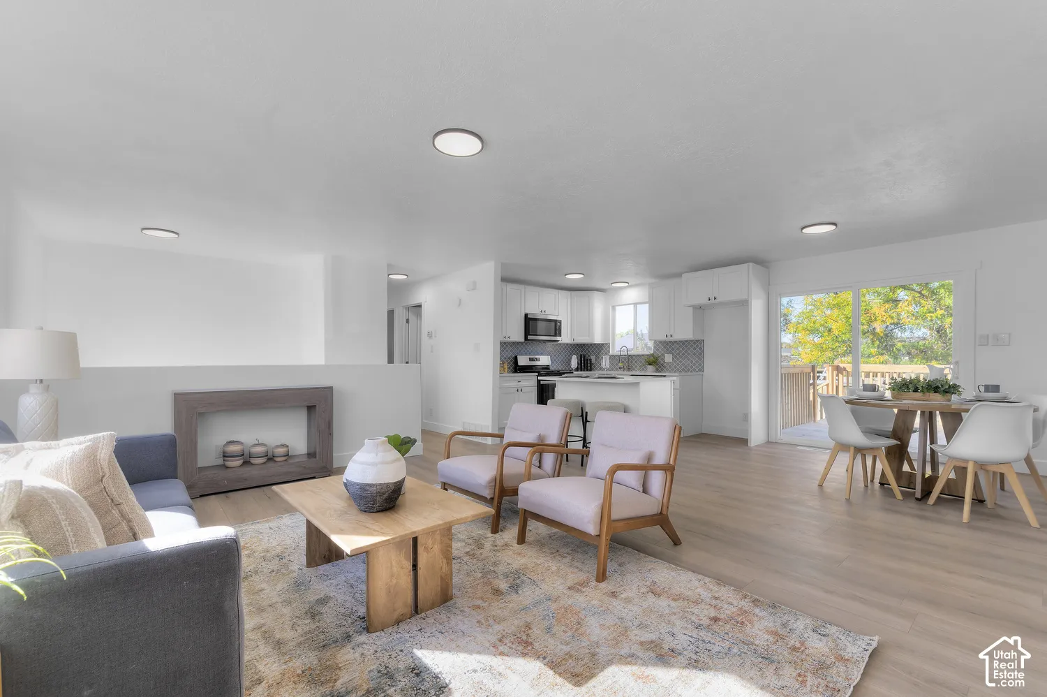 Open-concept interior featuring light-tone wood-finish flooring, recessed lighting, and kitchen cabinetry with a neutral tile backsplash
