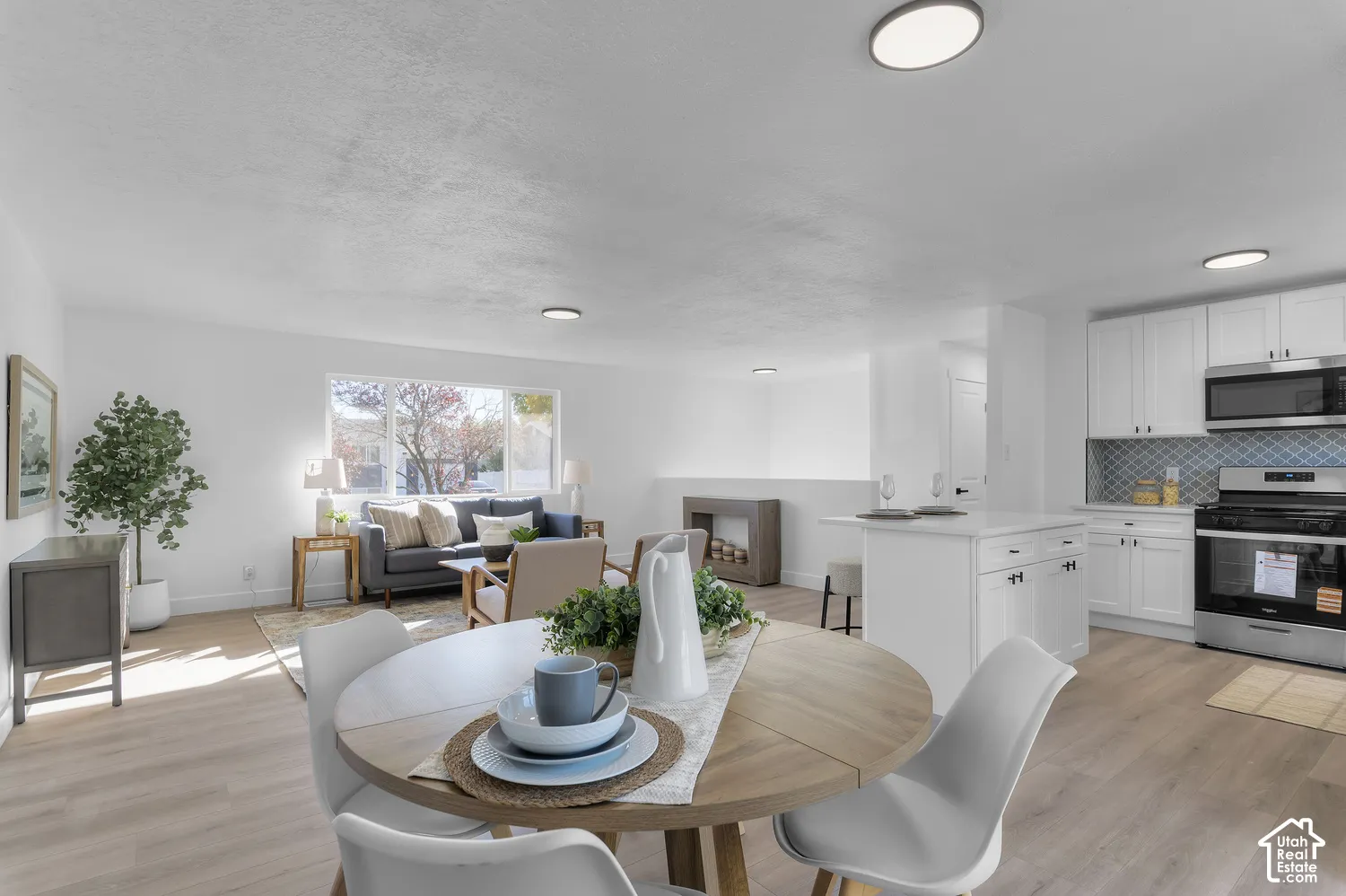 Open-concept living space featuring wood-finish flooring, a kitchen with white cabinetry, a center island with a quartz countertop, and a patterned tile backsplash