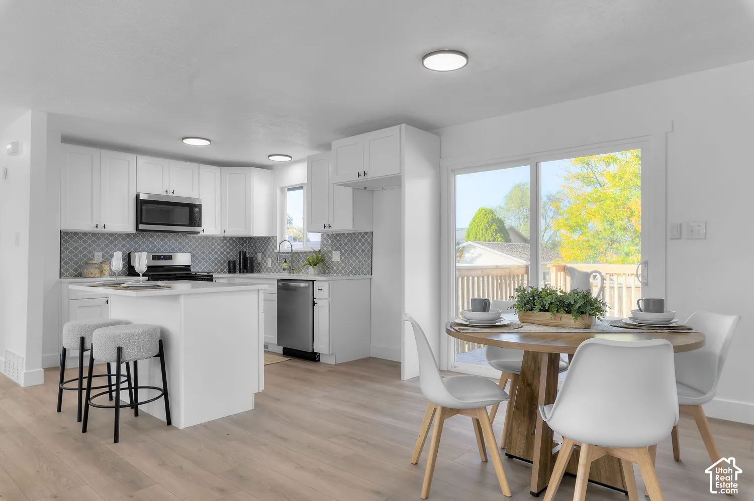 Kitchen featuring white shaker-style cabinetry, a central island with countertop seating, stainless steel appliances, patterned backsplash tile, and wood-finish flooring