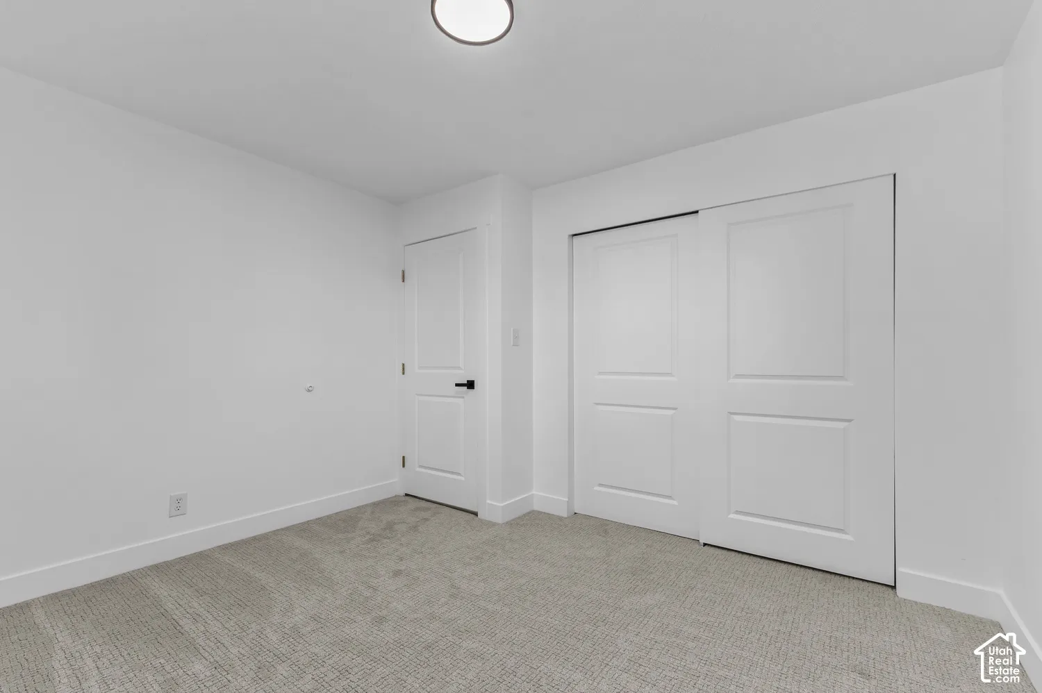 Neutral-toned carpeting, white walls, dual-panel interior door with matte black hardware, and sliding closet doors