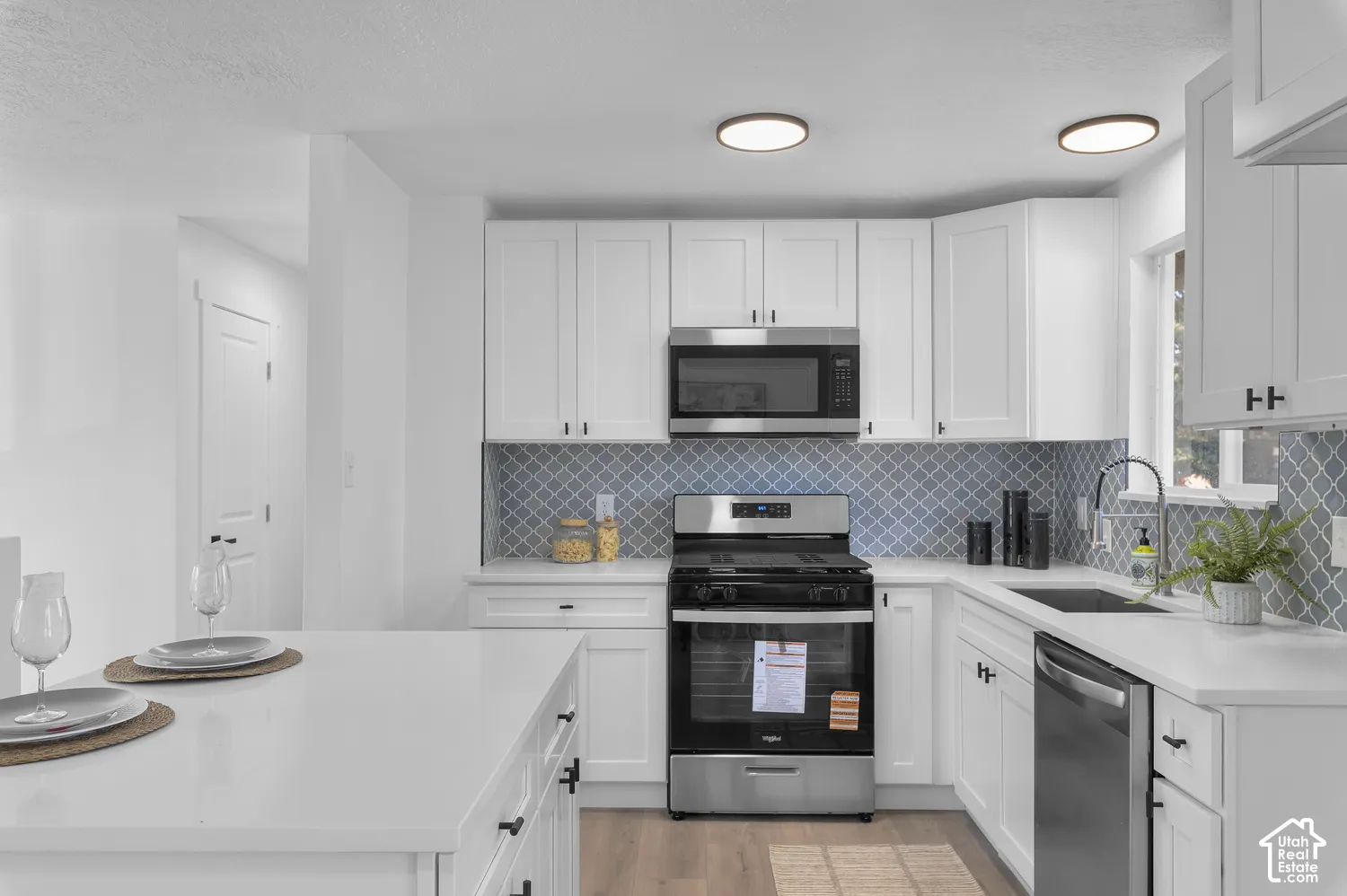 Kitchen featuring white cabinetry, quartz countertops, a patterned tile backsplash, stainless steel appliances, and wood-finish flooring