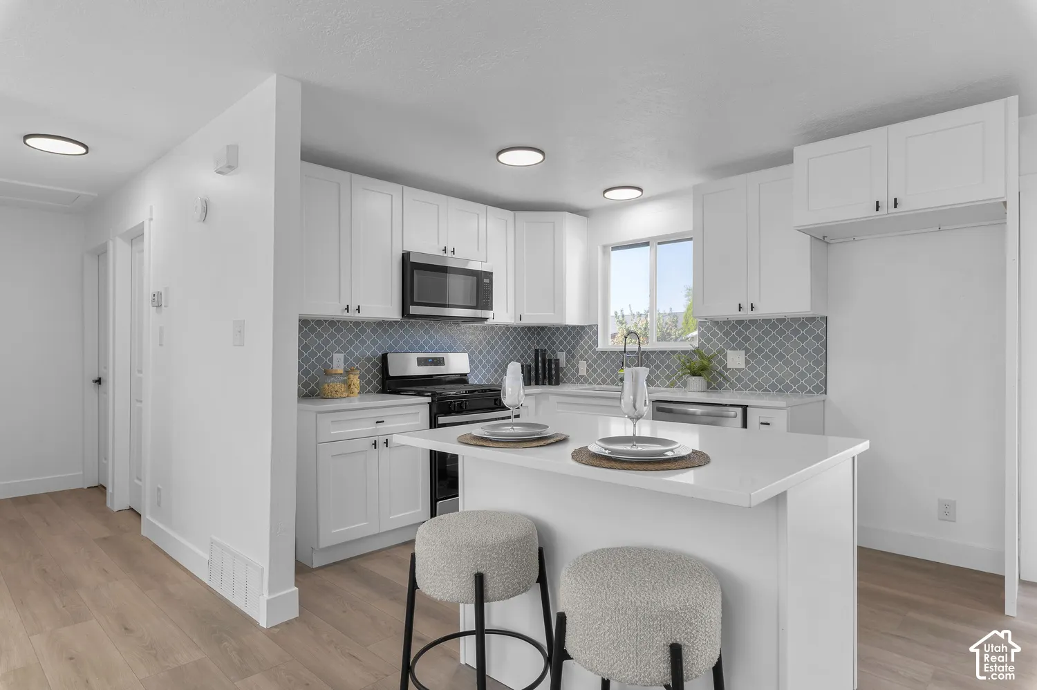 Kitchen featuring white cabinetry, quartz countertops, patterned tile backsplash, wood-finish flooring, and a center island