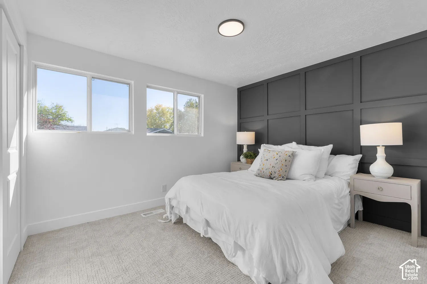 Charcoal-toned grid wall paneling, dual windows, neutral wall-to-wall carpeting, and a flush-mount overhead light fixture