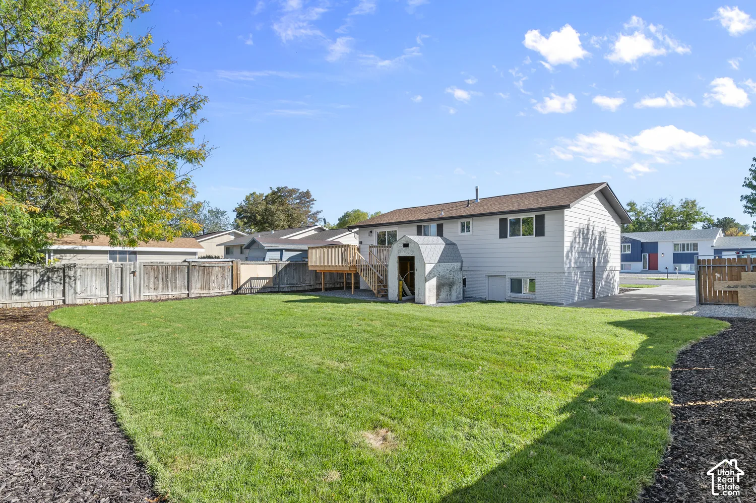 Backyard featuring a manicured lawn, wood-finish perimeter fencing, elevated wood deck, and detached storage structure