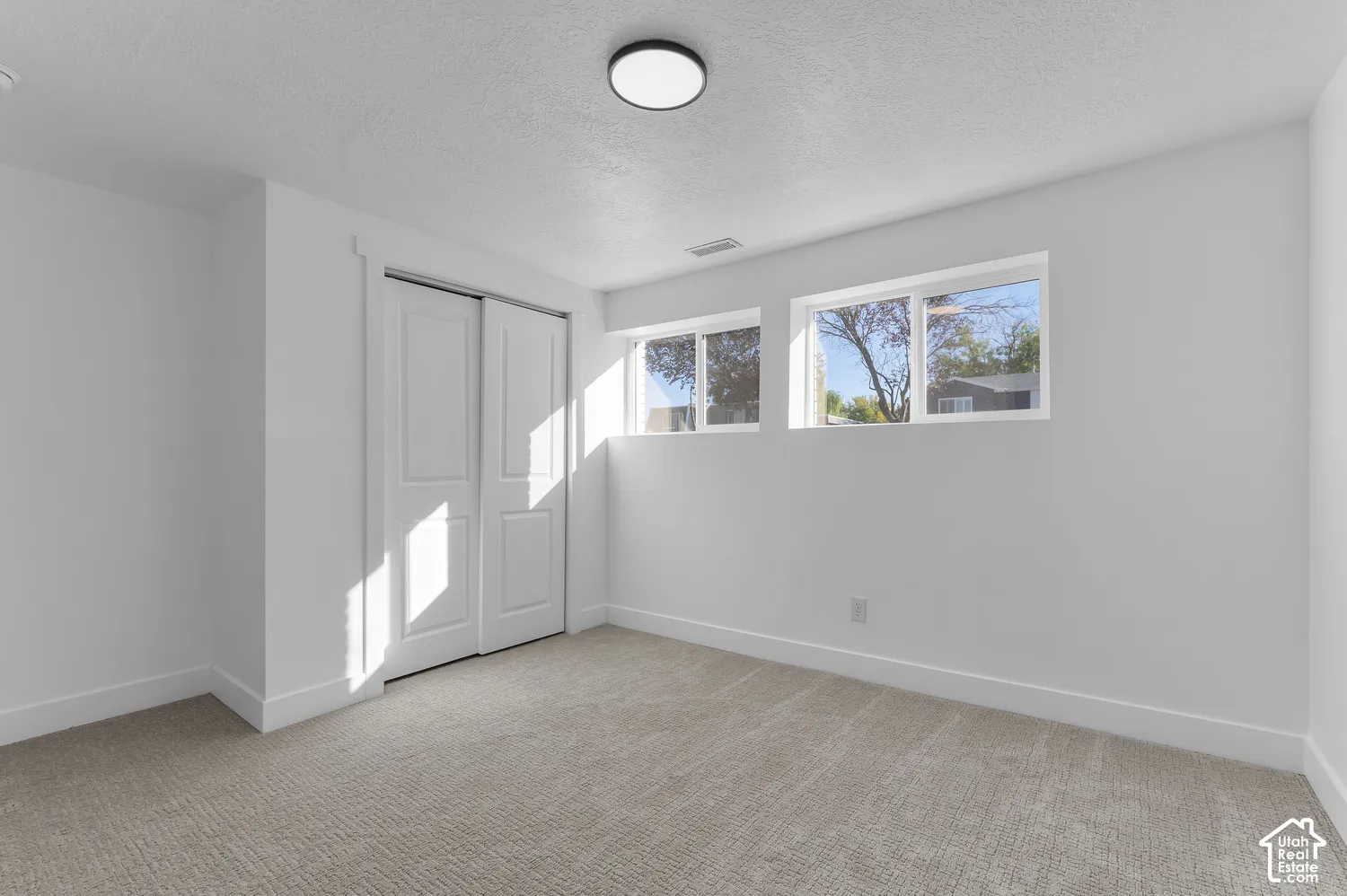 Neutral-toned carpeting, dual-pane windows, and a sliding door closet featuring a multi-panel design, illuminated by a ceiling-mounted flush light fixture