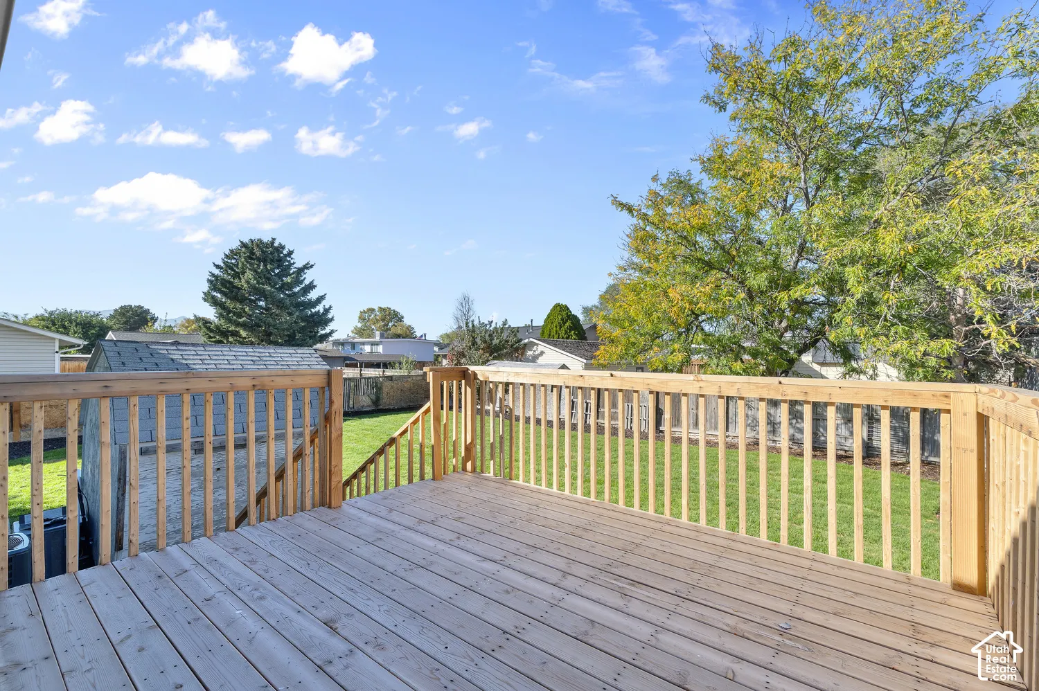 Raised wood deck with vertical baluster railing, stairs leading to a fenced backyard, and a detached storage shed