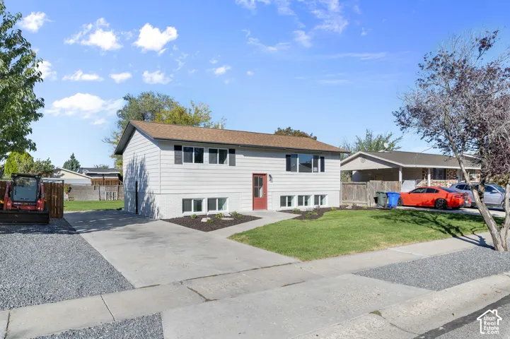 Exterior featuring light-toned horizontal siding, dark window shutters, concrete driveway, front lawn, and mature landscaping
